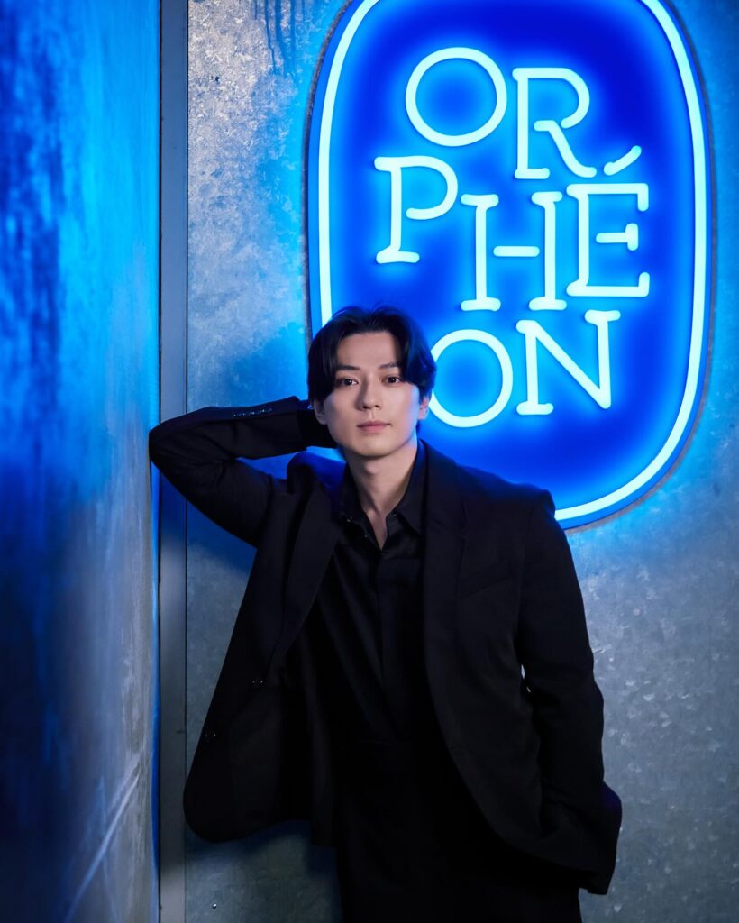 ORPHEONのロゴを背景に立つ新田真剣佑さんの写真