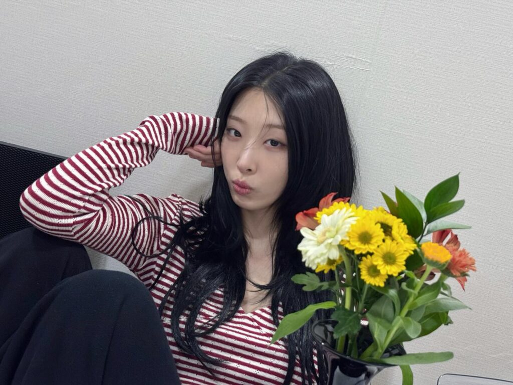 リュ・ダインさんが花瓶の花の前で室内に座りポーズを取る写真
