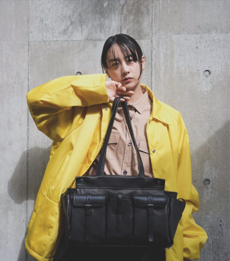 黄色いジャケットにPradaのカバンを持った山本美月さんの写真