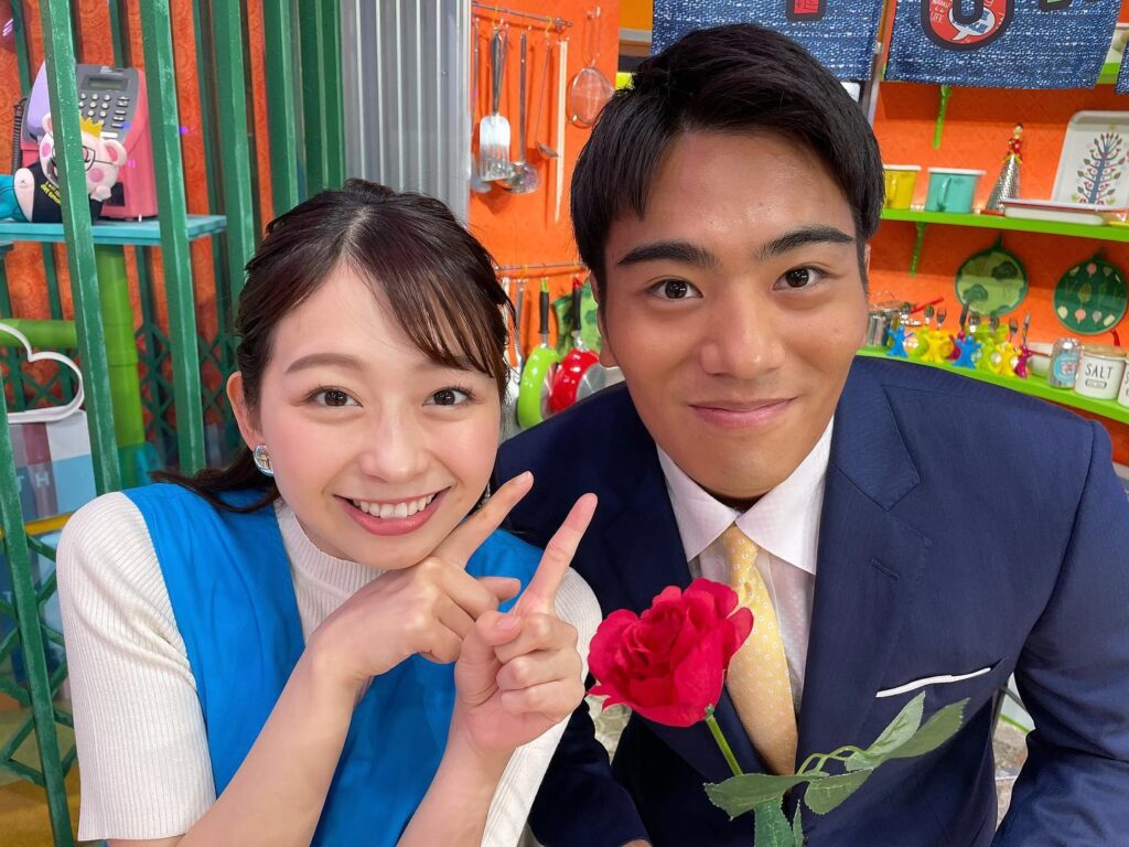 スタジオセットの中で、青い衣装の小室アナとスーツ姿の山本アナがカメラに向かって笑顔を見せている様子。