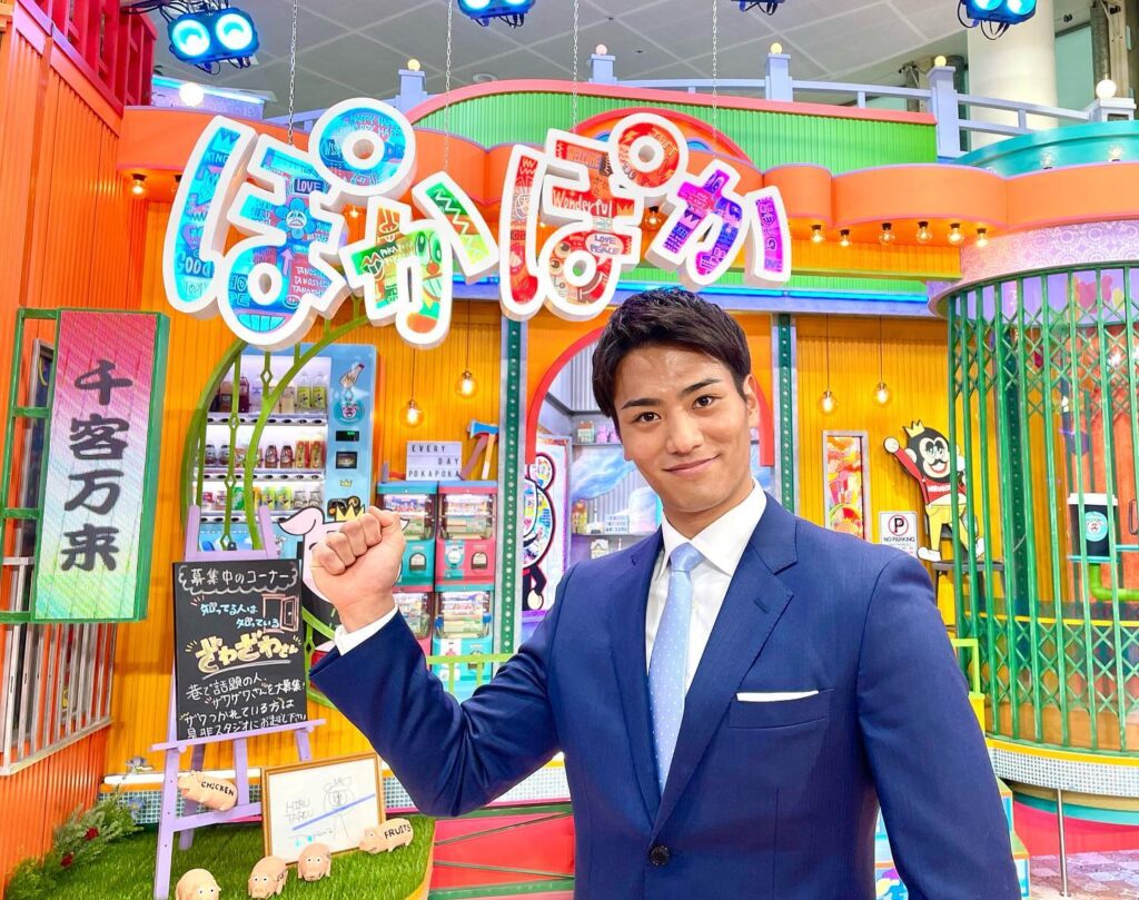 生放送バラエティ「ぽかぽか」の撮影スタジオでスーツ姿の山本アナがガッツポーズをしている様子。