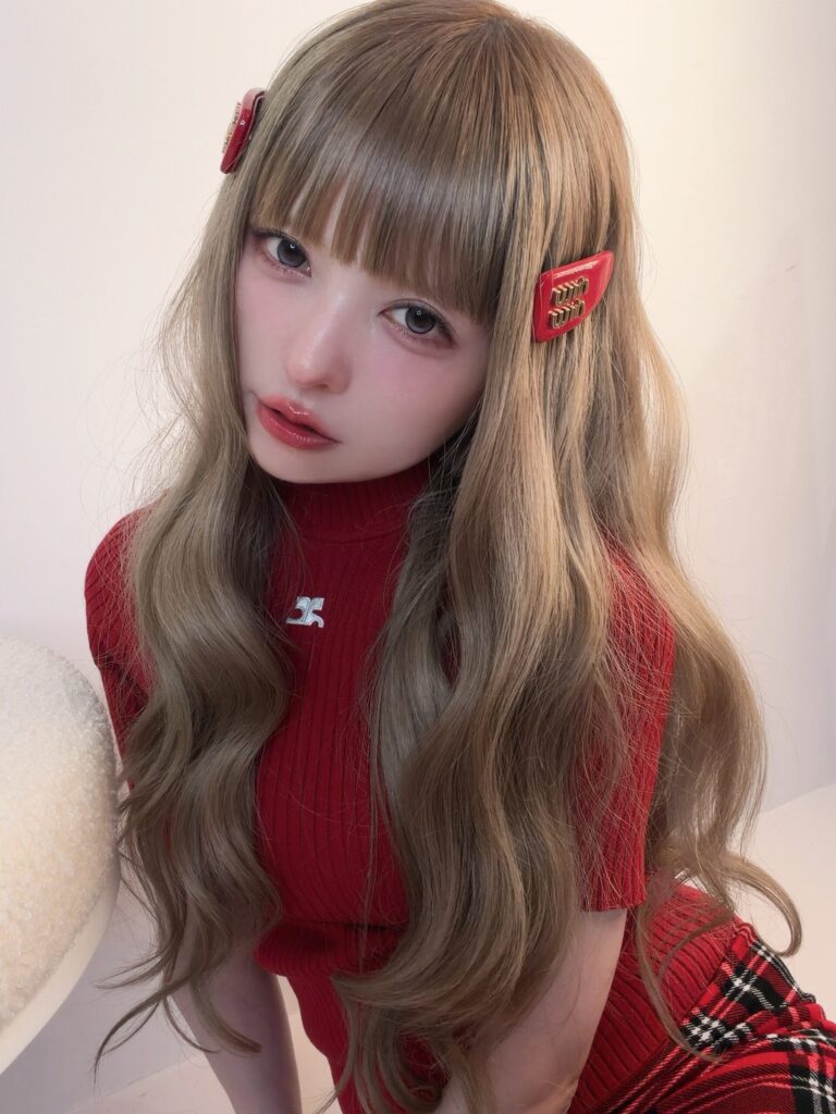 赤いヘアクリップを付けたロングヘアの益若つばささんが、赤いハイネックニットを着てこちらを見つめているポートレート写真