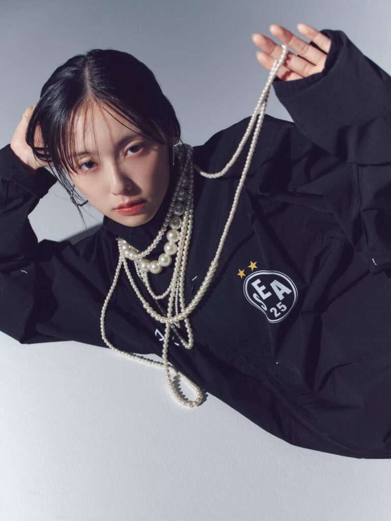 パールネックレスを手に持ち、黒いトップス姿でポーズをとる加藤小夏さん